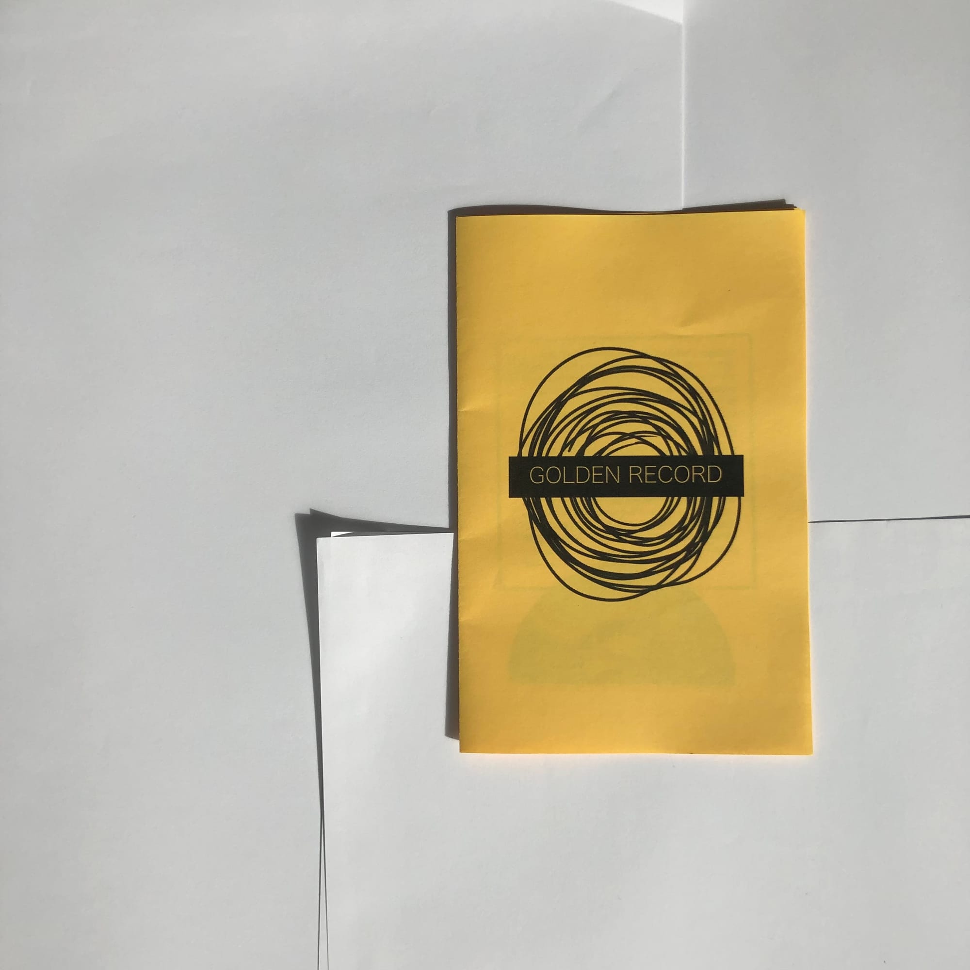 goldenrod coloured folded paper zine printed with black ink. the cover is a circular swirl of lines and the title "Golden Record"